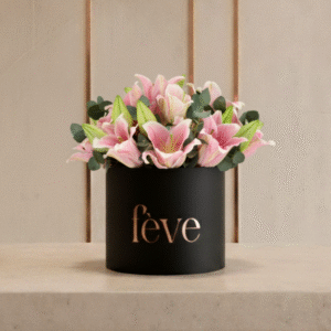 A black cylindrical box with the word “fève” in rose-gold lettering holds an arrangement of pink lilies