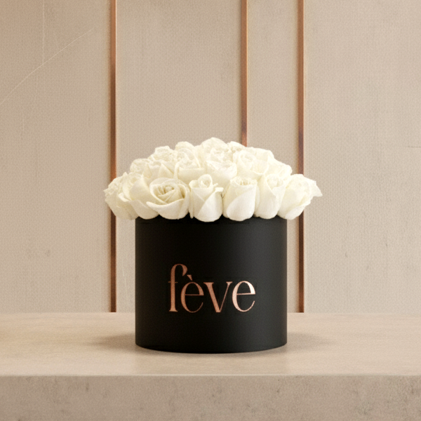 A black cylindrical box filled with tightly arranged white roses sits on a light stone surface.