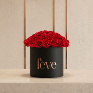 A black cylindrical box with the word “fève” in rose-gold lettering is filled with a tightly arranged dome of deep red roses.