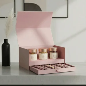 Luxury pastel pink gift box by Feve featuring three jars of gourmet treats and a pull-out drawer of assorted chocolate truffles in a minimalist setting.