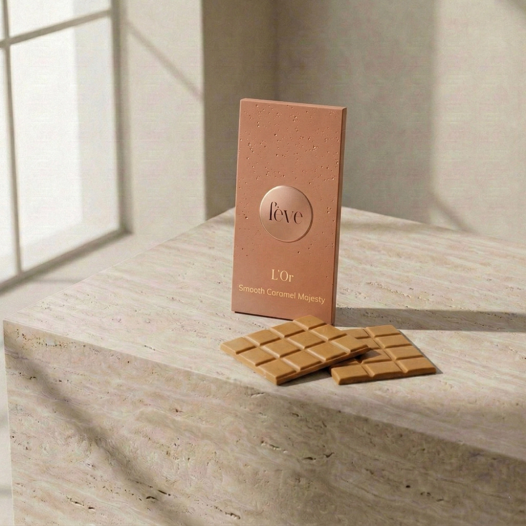 Luxury fève L’Or caramelized chocolate bar and two squares of Smooth Caramel Majesty on a minimalist travertine stone surface