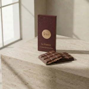 Fève Le Fraisier milk chocolate bar with strawberry cheesecake ganache filling, broken to show the crimson center on a luxury stone surface.