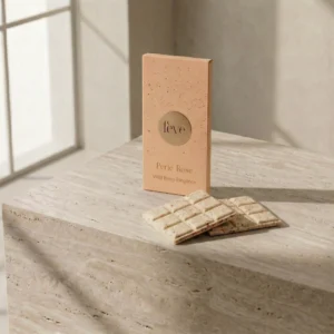 Fève Perle Rose Wild Berry Elegance chocolate bar packaging and speckled white chocolate squares on a travertine stone pedestal.