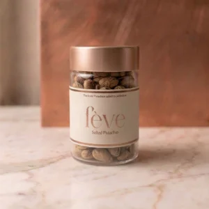 Fève gourmet salted pistachios in a luxury glass jar with a rose gold lid, displayed on a marble surface.