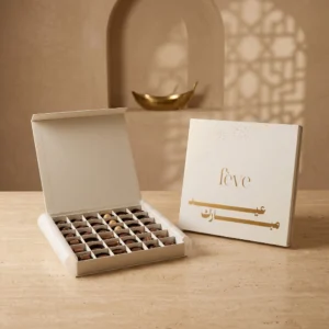 A luxury 36-piece chocolate box from the fève Zénith collection, featuring assorted milk chocolates and white pralines, displayed next to a white and gold Eid Mubarak gift box lid.